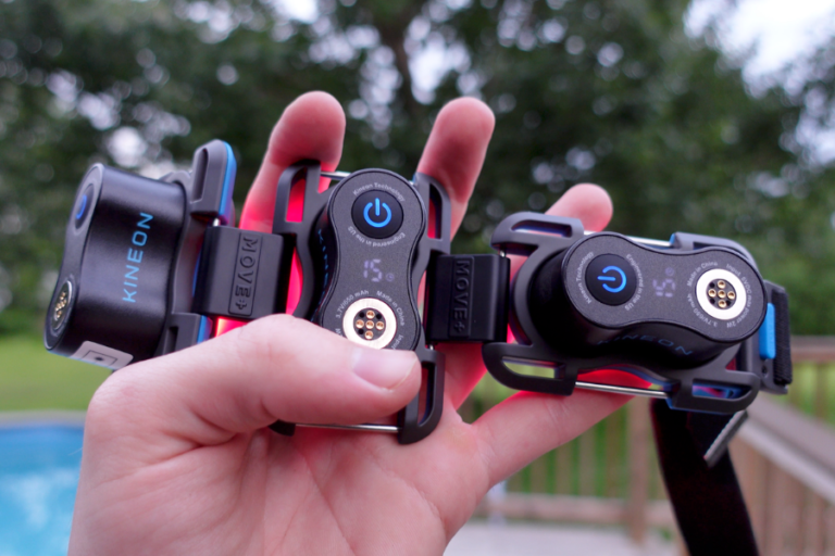 Three Kineon Move+ red light therapy modules held in one hand outdoors, showing the power button, LED display, and elastic strap system.