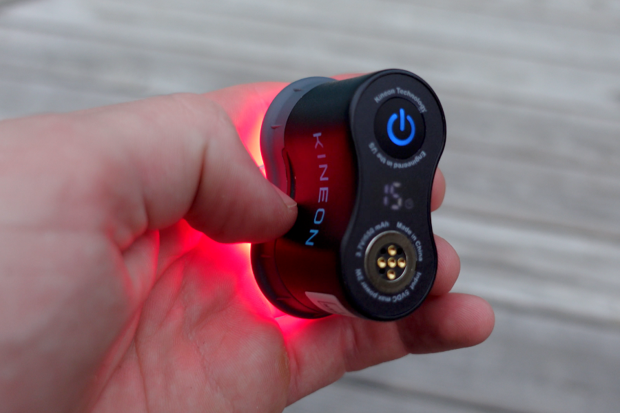 Single Kineon Move+ red light therapy module held in hand showing red light emission and power button