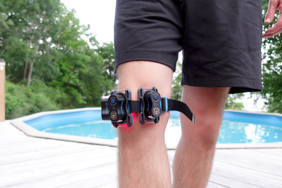 Two Kineon Move+ red light therapy modules strapped to a man's knee while standing on a deck