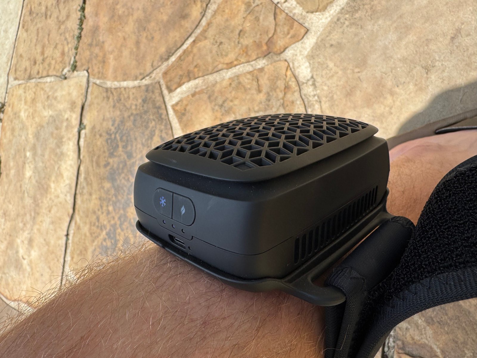 Side view of the Therabody RecoveryTherm Cube strapped to a leg, showing the control panel with snowflake (cool) and flame (heat) buttons, three blue LED battery indicator lights, and USB-C charging port.