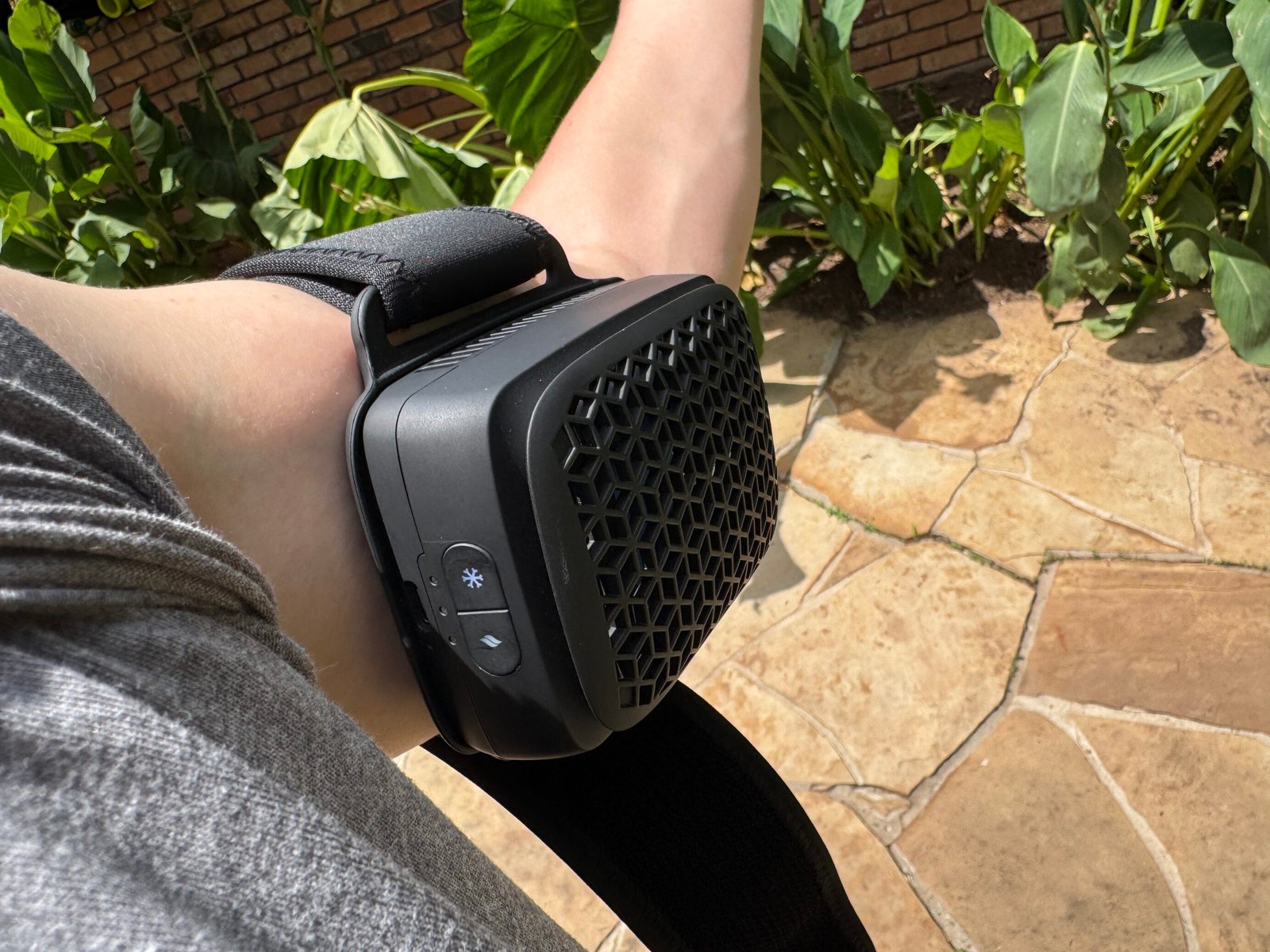 Person wearing the Therabody RecoveryTherm Cube strapped to their bicep outdoors, showing the device secured with the wrap strap in a typical use position.